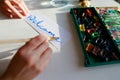 Young woman painter writes watercolor writing on paper, sitting