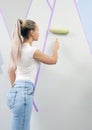 Young woman painting wall with paint roller and using masking tape while standing on ladder Royalty Free Stock Photo