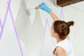 Young woman painting wall with paint roller and using masking tape while standing on ladder Royalty Free Stock Photo