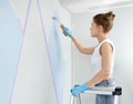 Young woman renovating home painting wall with paint roller and using masking tape while standing on ladder Royalty Free Stock Photo