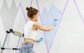 Young woman painting wall with paint roller and using masking tape while standing on ladder Royalty Free Stock Photo