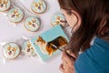 Young woman paints with brush handmade gingerbreads with welsh corgi dog portraits, cardboard box is near. Beautiful cookies decor