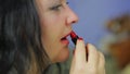 Young woman paints lips with bright red lipstick. Profile.