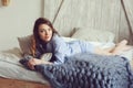 Young woman in pajama wake up in the morning in cozy scandinavian bedroom and lying on bed with oversize knitted blanket Royalty Free Stock Photo
