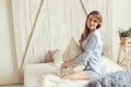 Young woman in pajama wake up in the morning in cozy scandinavian bedroom and lying on bed with oversize knitted blanket Royalty Free Stock Photo