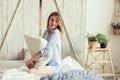 Young woman in pajama wake up in the morning in cozy scandinavian bedroom and lying on bed with oversize knitted blanket Royalty Free Stock Photo