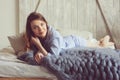 Young woman in pajama wake up in the morning in cozy scandinavian bedroom and lying on bed with oversize knitted blanket Royalty Free Stock Photo