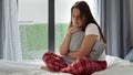 The young woman in pajamas huddled on the bed, holding and embracing a cushion for comfort. The concept of sadness, emotional pain