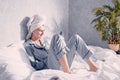 Young woman in pajamas and a towel on her head sits in bed and looks at her phone Royalty Free Stock Photo