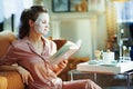 Young woman with white sheet facial mask reading book