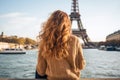 Young woman in Paris looking at the Eiffel Tower, France, Young traveler woman rear view sitting on the quay of Seine River