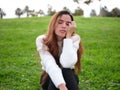 A young woman in the park sitting on the grass with one hand on her face falling asleep. Royalty Free Stock Photo