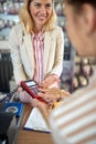 Young woman paying with credit card, entering her pin code, lovely smiling sales person holding credit card reader for customer Royalty Free Stock Photo