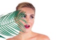 Young woman perfect skin make-up with long eyelashes and red lipstick holding a tropical palm leaf closeup shoulders Royalty Free Stock Photo