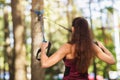 Young woman performs an exercise to work out the muscles of the back with fitness straps attached to a tree in the park