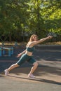 Young woman performs leg lunges on a street sports ground.