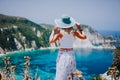 Young woman on Petani beach Kefalonia, holding blue sunhat enjoying picturesque panorama of emerald azure bay lagoon