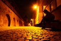 Young woman with a phone in hand, on a bench, late at night, on a medieval style cobblestone street in Sibiu, Romania