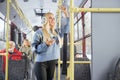 Young woman with phone holding handle standing inside moving bus in winter.