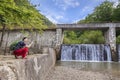 Young woman photographing a small dam with a waterfall