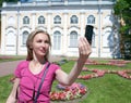 Young woman photographs herself on the cell phone against pavilion Stone hall in Oranienbaum, Petersburg, Russia