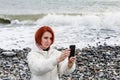 Young woman photographs herself on the phone against the backdrop of the sea waves Royalty Free Stock Photo