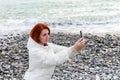 Young woman photographs herself on the phone against the backdrop of the sea waves Royalty Free Stock Photo