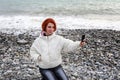 Young woman photographs herself on the phone on seacoast against the backdrop of the sea waves Royalty Free Stock Photo