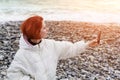 Young woman photographs herself on the phone on seacoast against the backdrop of the sea waves at sunset Royalty Free Stock Photo