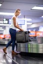 Young woman picking up suitcase from baggage claim conveyor belt in an airport terminal Royalty Free Stock Photo