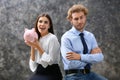 Young woman with piggy bank and her displeased husband on grey background Royalty Free Stock Photo