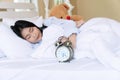 Young woman on pillow with teddy bear sleeping rest on the white bed with handles the alarm clock in her hand in the Royalty Free Stock Photo