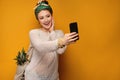 Young woman with a pineapple in her shopping bag takes a selfie over yellow background Royalty Free Stock Photo