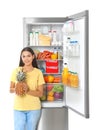 Young woman with pineapple near open refrigerator