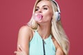 Beautiful blonde woman blowing pink bubble gum. Girl listen music in headphones. Fashion and lifestyle portrait. Royalty Free Stock Photo