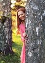 Young woman in pink dress, peek a boo behind the tree, with suns