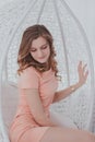 A young woman in a pink dress sitting in a white hanging chair Royalty Free Stock Photo