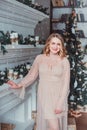 A young woman in a pink dress standing by the fireplace on the background of a Christmas tree Royalty Free Stock Photo