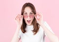 Young woman in pink glasses is very surprised looking at the camera and lowering her glasses. Surprise and shopping concept on Royalty Free Stock Photo