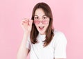 Young woman in pink glasses is very surprised looking at the camera and lowering her glasses. Surprise and shopping concept on Royalty Free Stock Photo