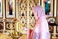 Young woman in pink headscarf praying near candles at wooden church. Female person worship God in temple Royalty Free Stock Photo