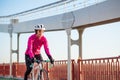 Young Woman in Pink Jacket Riding Road Bicycle on the Bridge Bike Line in the Cold Sunny Autumn Day. Healthy Lifestyle.