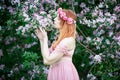 Young woman in a pink lace dress and a wreath of roses inhales the fragrance of a flowering tree. An idea for a photo shoot Royalty Free Stock Photo