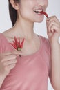 Young woman in pink shirt eating a chili pepper, studio shot, half face showing Royalty Free Stock Photo