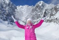 Mladá žena v ružovej lyžiarskej bunde, rukaviciach a zimnej čiapke, usmieva sa, hádže sneh do vzduchu, slnko svieti na horu za ňou.