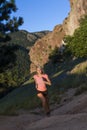 Young woman in pink top running up steep hill with mountain vista.