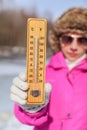 Young woman in pink winter jacked, gloves and furry hat holding thermometer that is showing -5 degrees. Winter / cold days coming Royalty Free Stock Photo