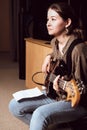 young woman playing bass guitar and reading chord notes at band rehearsal. vertical size. studio sound check. woman