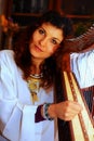 Young woman playing celtic harp in a white angelic historical costume.