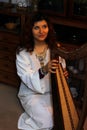 Young woman playing celtic harp in a white angelic historical costume.